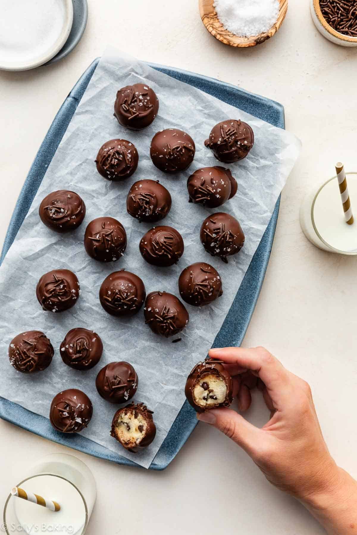 cookie dough truffles covered in chocolate and topped with chocolate sprinkles and sea salt on blue plate.