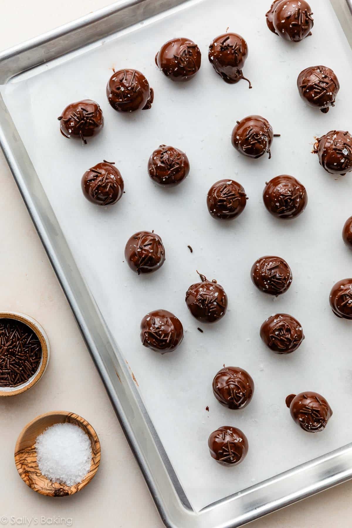 truffles topped with chocolate sprinkles and sea salt on parchment paper-lined baking sheet.