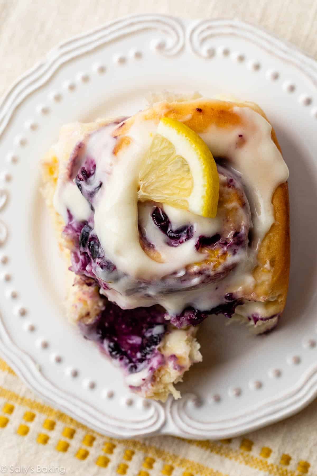 blueberry lemon sweet roll with cream cheese icing on a white plate.