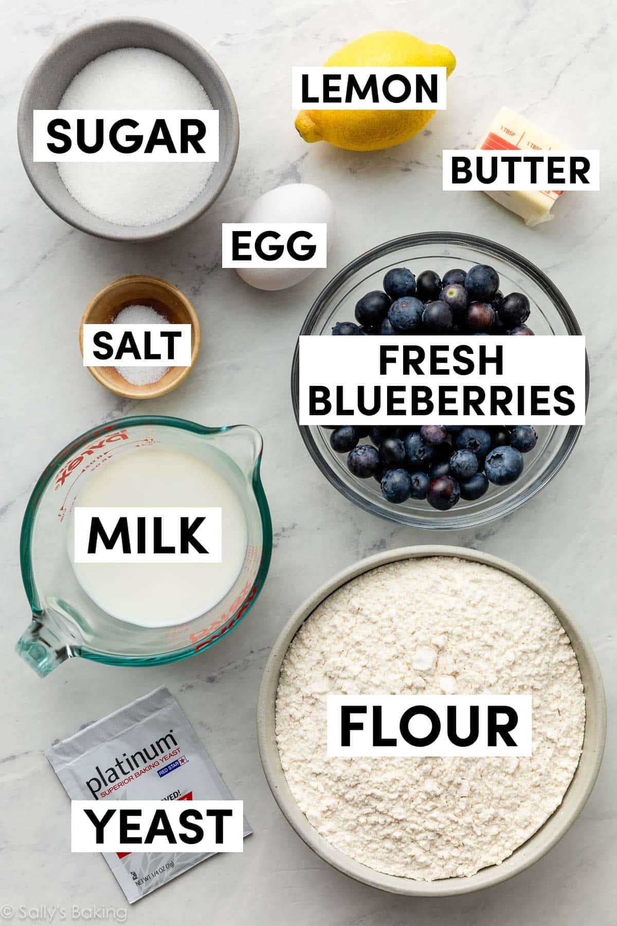 ingredients in bowls including sugar, lemon, flour, milk, yeast, salt, and egg.