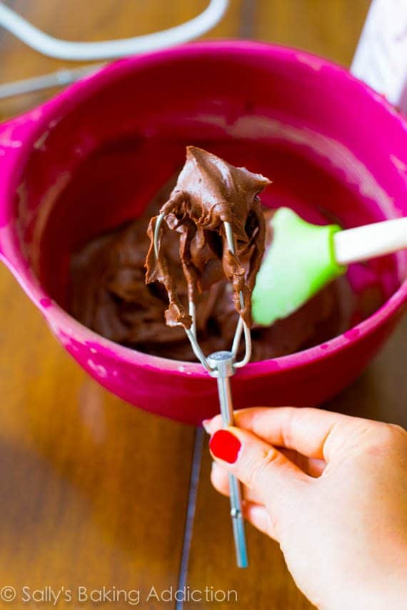 hand holding a beater with dark chocolate frosting on it