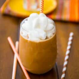 pumpkin frappuccino in a glass with whipped cream and a straw