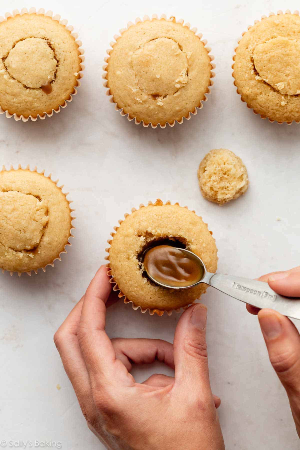 filling a cupcake with butterscotch sauce.
