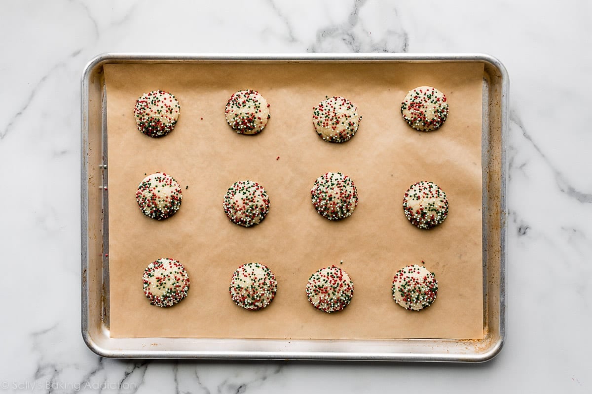 sugar cookies coated in holiday colored nonpareil sprinkles on lined baking sheet.