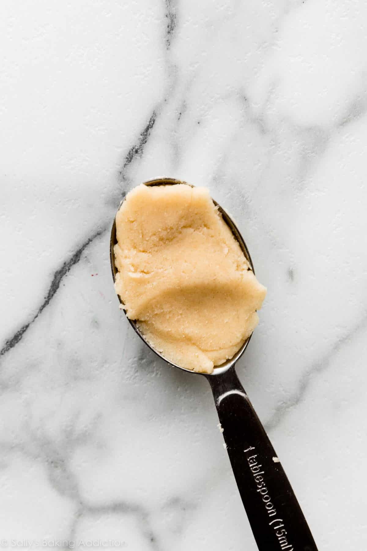 Tablespoon measuring spoon with vanilla cookie dough in it.