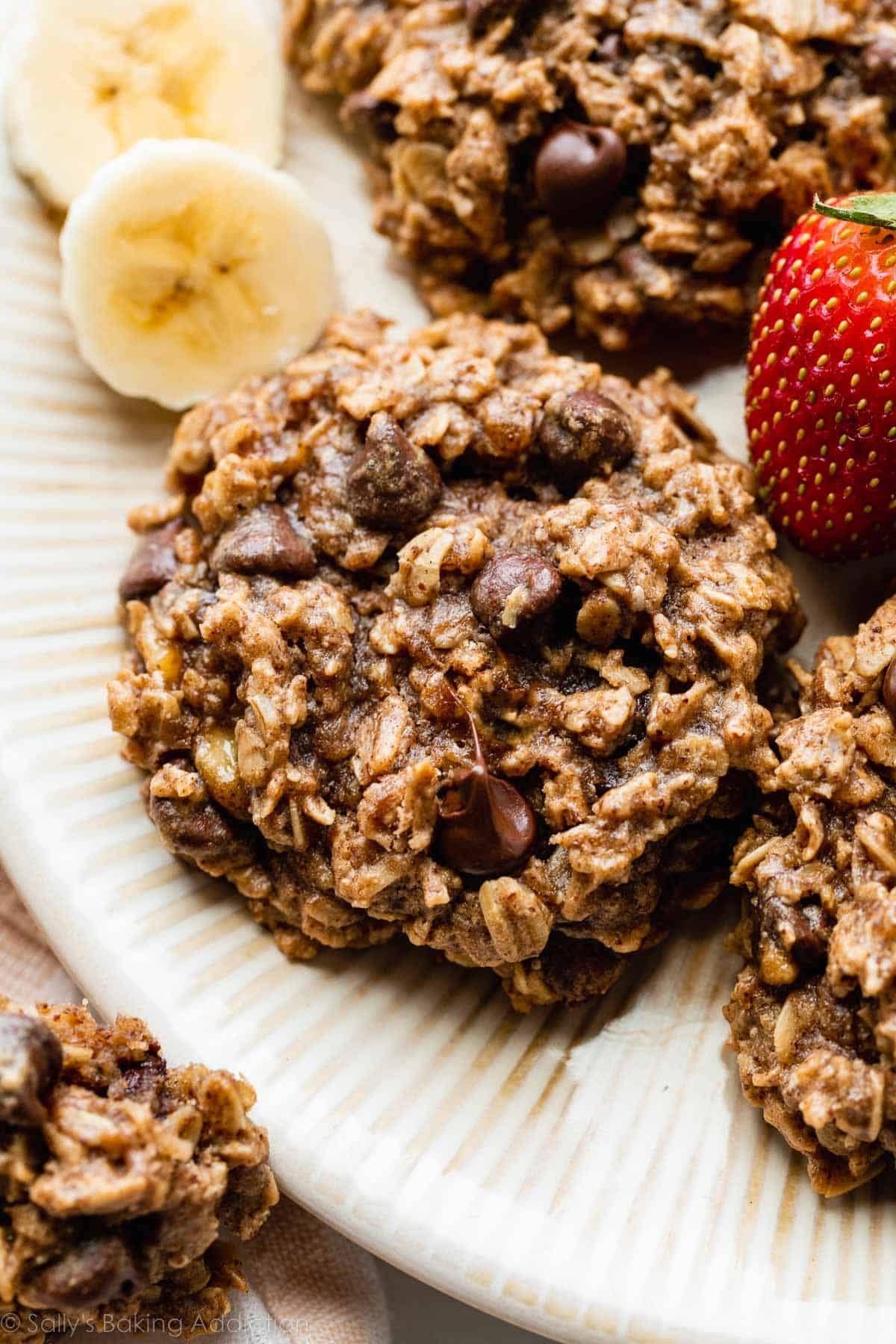 banana chocolate chip breakfast cookie on plate with strawberry and banana slices.