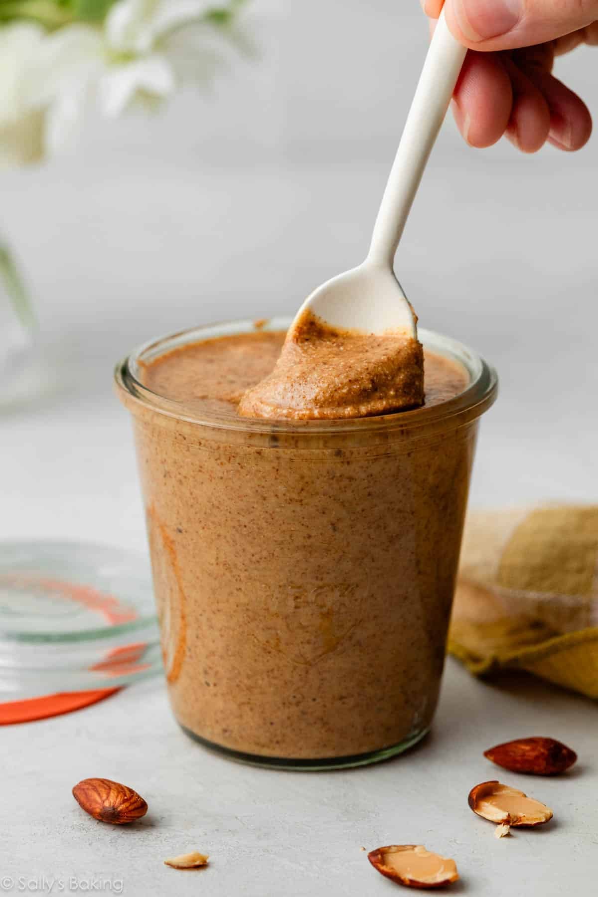 homemade almond butter in glass jar with white spoon.