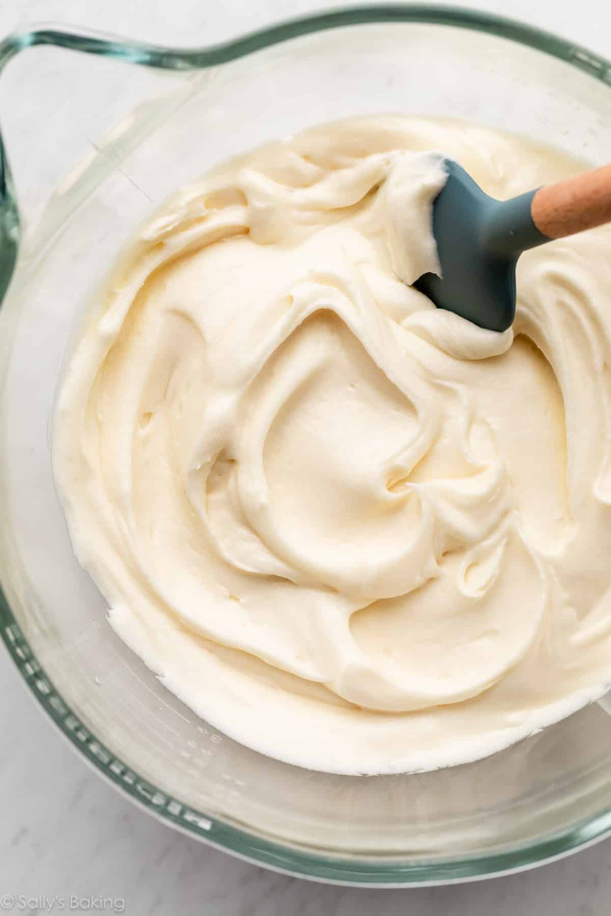 cream cheese frosting in glass bowl with blue spatula.