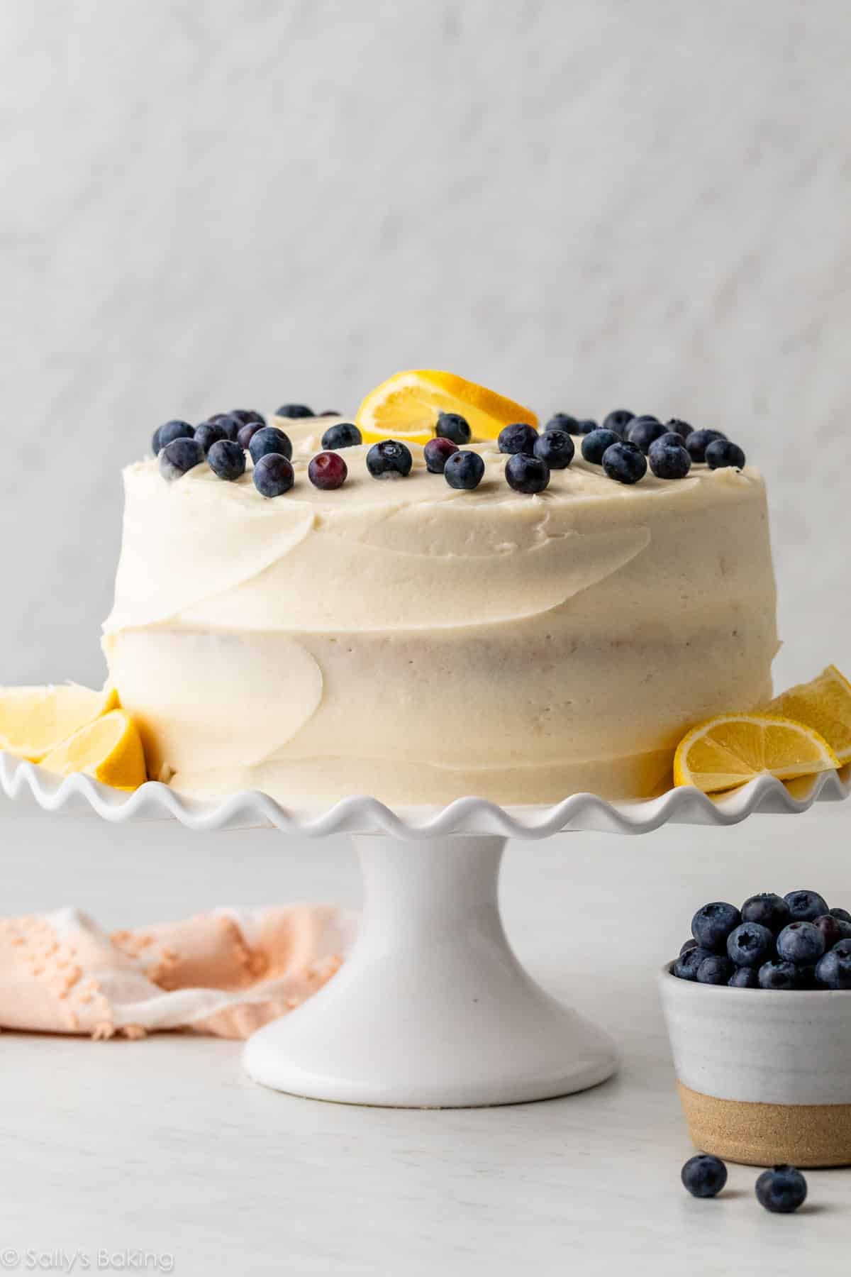 lemon blueberry layer cake with cream cheese frosting on a white cake stand.