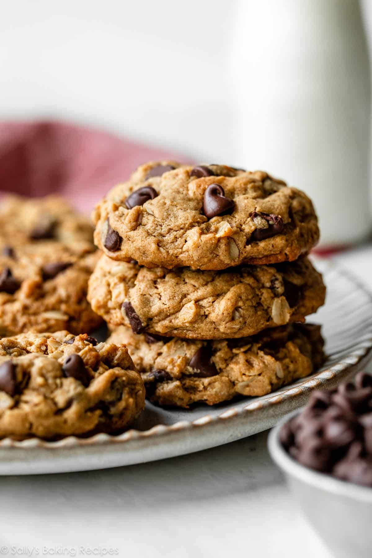 stack of 3 peanut butter oatmeal cookies on gray plate with glass of milk in background.