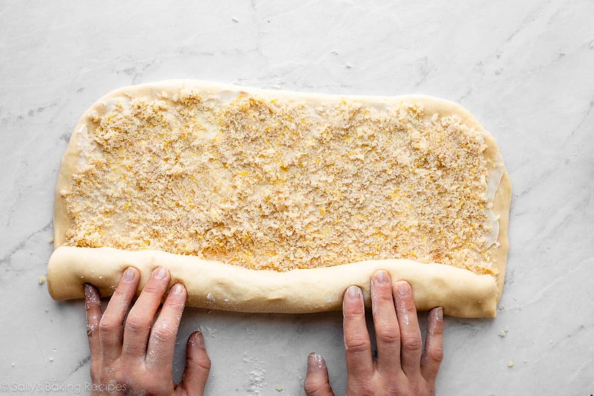 hands rolling up filled dough, cinnamon roll style.