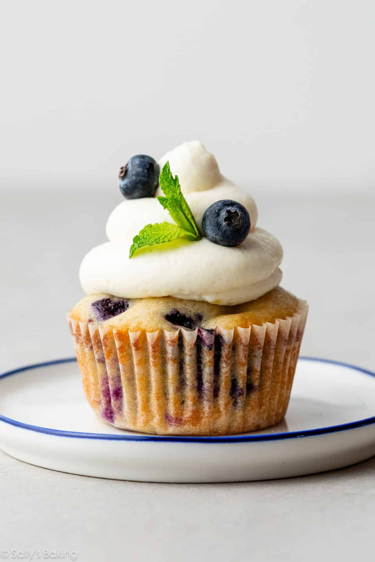 blueberry cupcake with whipped cream cheese frosting on top with fresh mint.