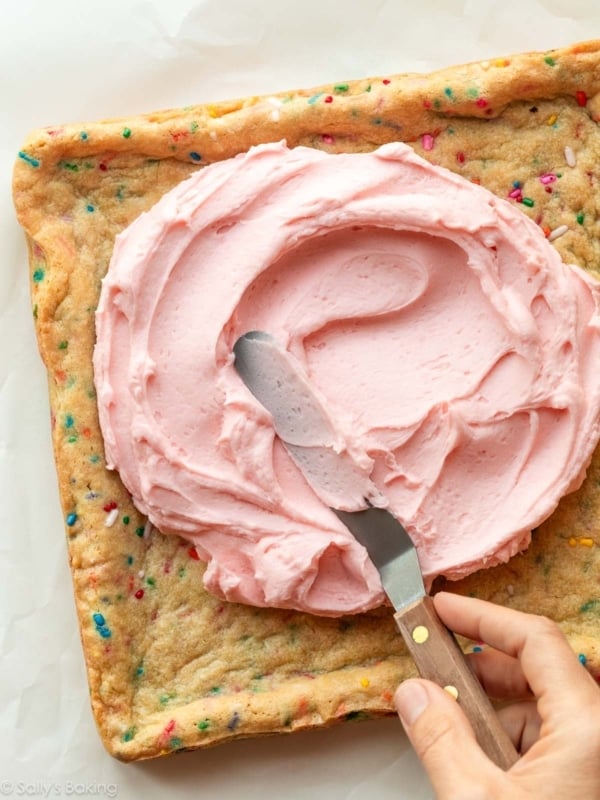 spreading pink frosting on sprinkle bars.