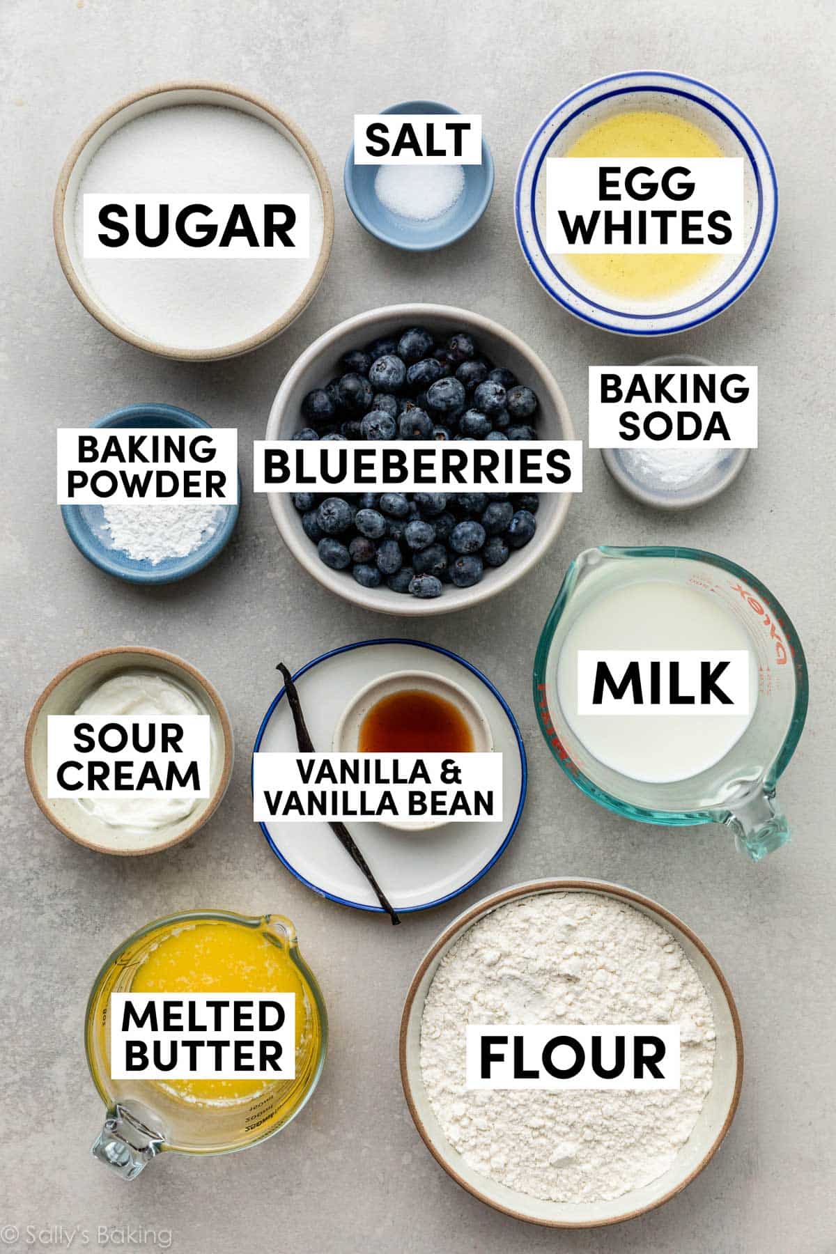ingredients measured out in cups including melted butter, flour, milk, egg whites, blueberries, baking powder, baking soda, and sugar.