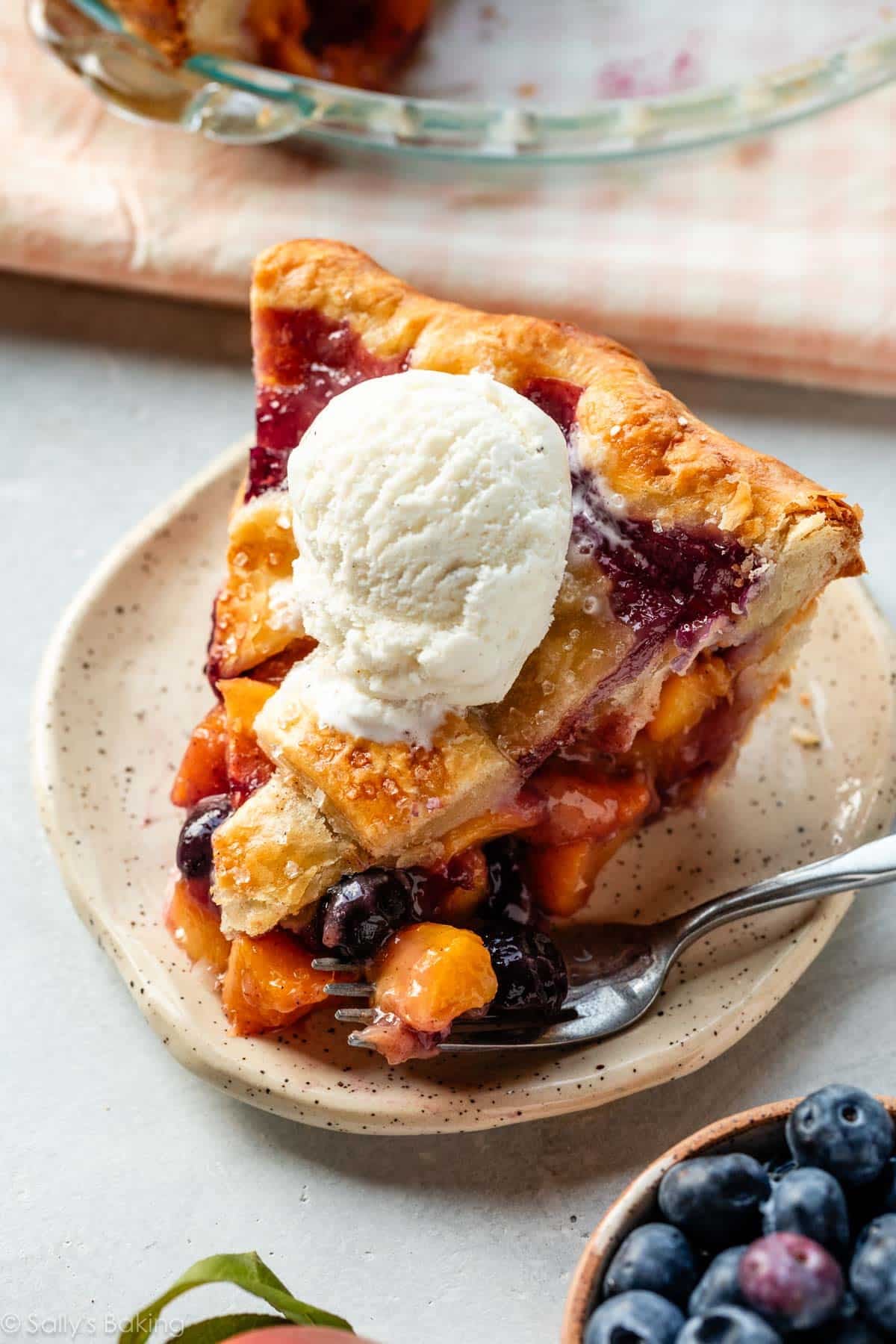 slice of blueberry peach pie with vanilla ice cream on top.