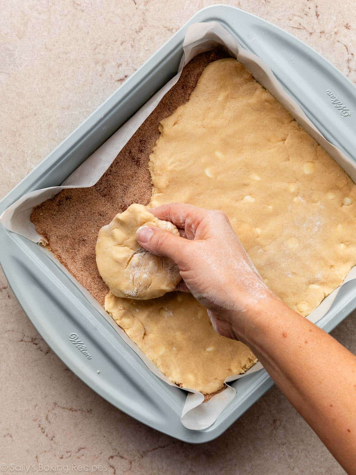 hand placing flattened dough on top of cinnamon sugar mixture.