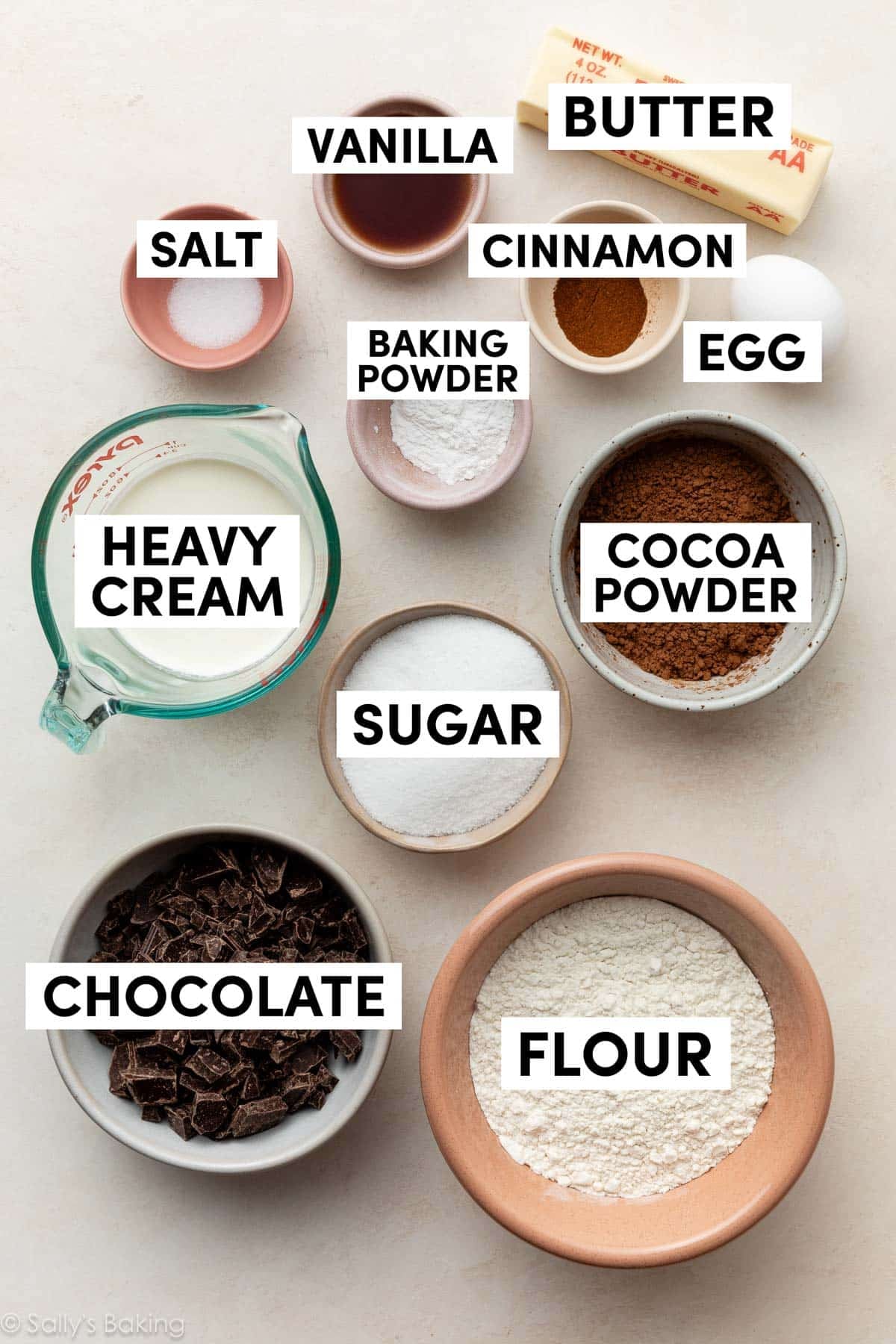 ingredients in bowls including chocolate, sugar, cocoa powder, cream, and cinnamon.