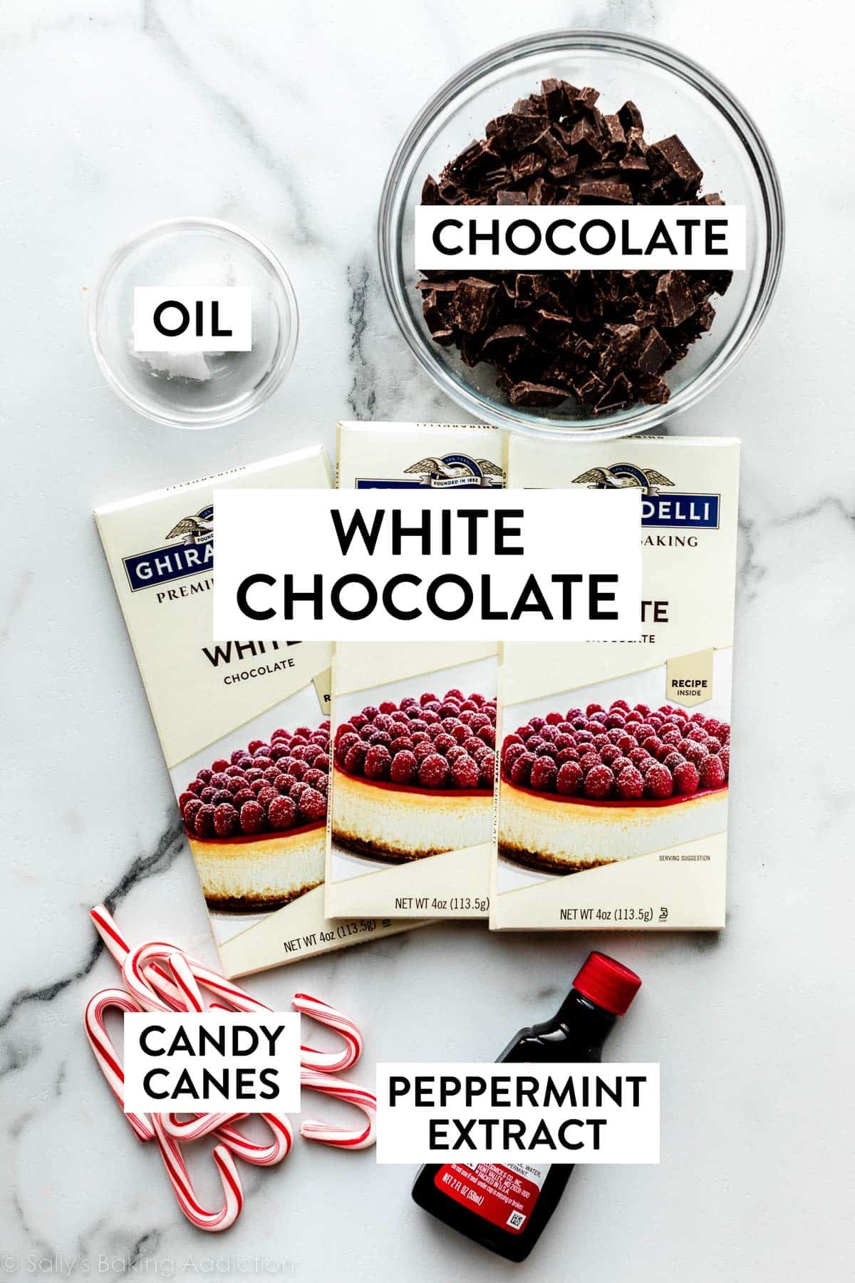 ingredients on counter including 3 white chocolate bars, bowl of chopped chocolate, small bowl of coconut oil, candy canes, and peppermint extract.