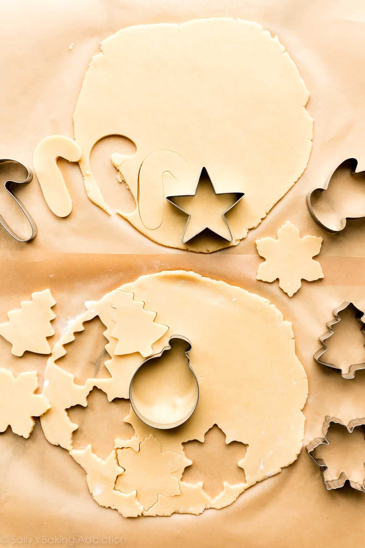 two slabs of rolled out dough on parchment paper with cookie cutters cutting out shapes.
