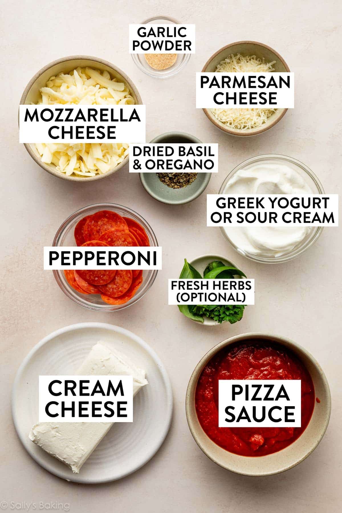 ingredients in bowls including parmesan cheese, garlic powder, mozzarella cheese, pizza sauce, pepperoni, and fresh herbs.