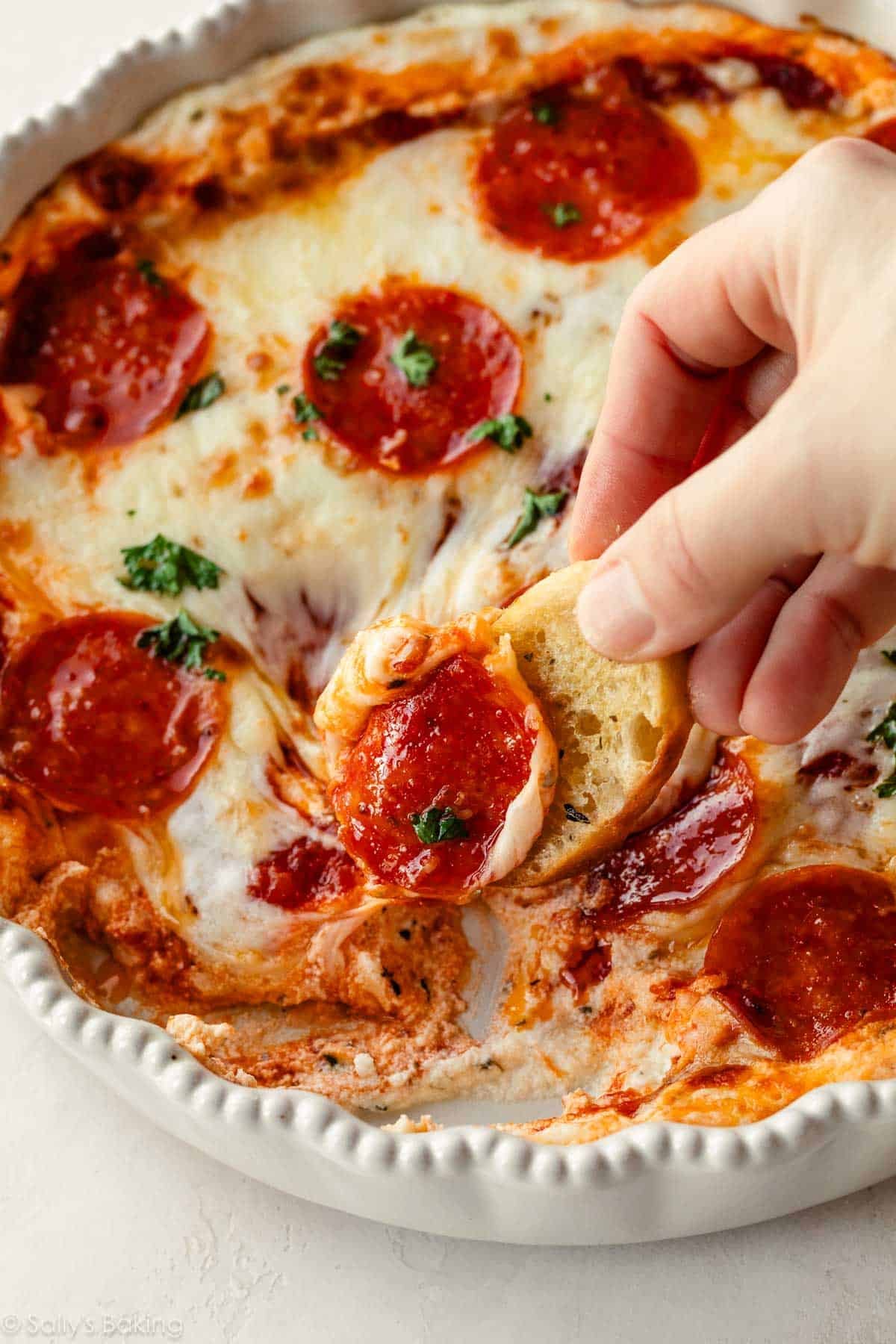 crostini being dipped in pizza dip with pepperonis on top.
