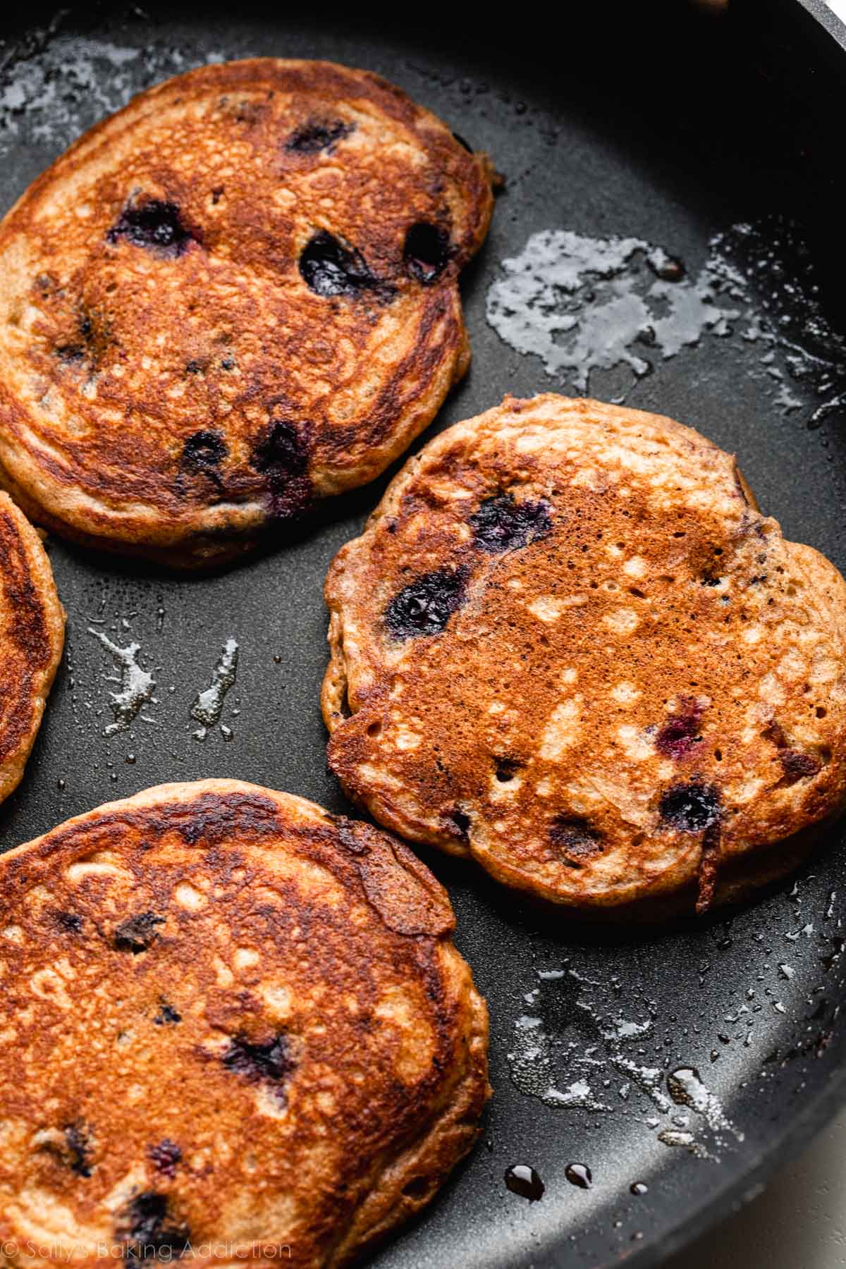 3 blueberry pancakes being cooked in skillet.