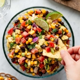 hand dipping a tortilla chip in black bean corn avocado salsa.