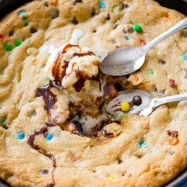 M&Ms chocolate chip skillet cookie topped with ice cream in a blue skillet with spoons