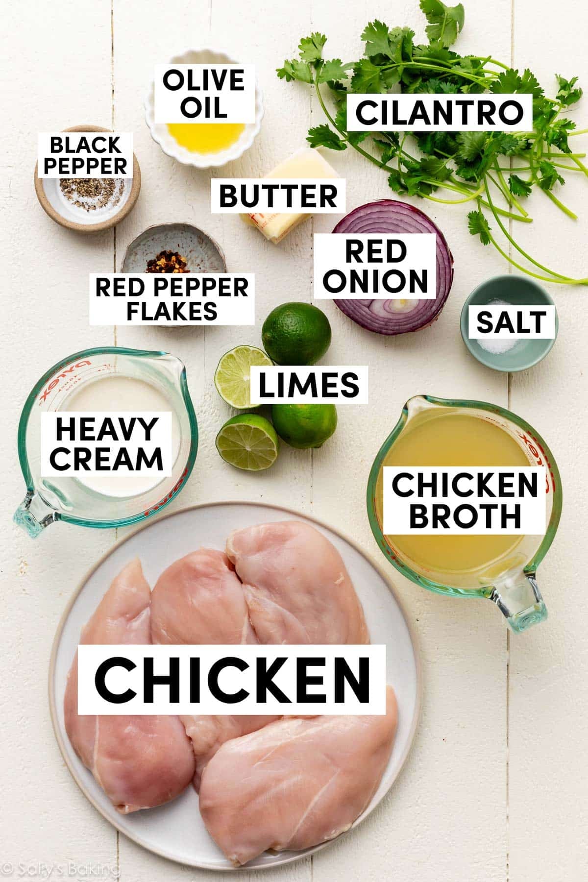 ingredients on white wood surface including chicken broth, red onion, chicken, heavy cream, red pepper flakes, olive oil, and butter.