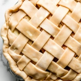 pie crust in lattice design on top of apple pie sitting in glass pie dish.