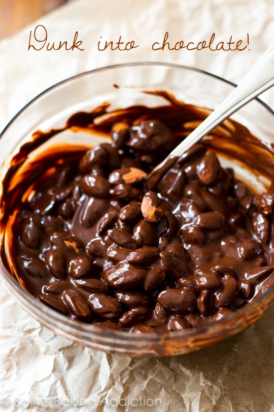 almonds in a glass bowl of melted dark chocolate with a spoon