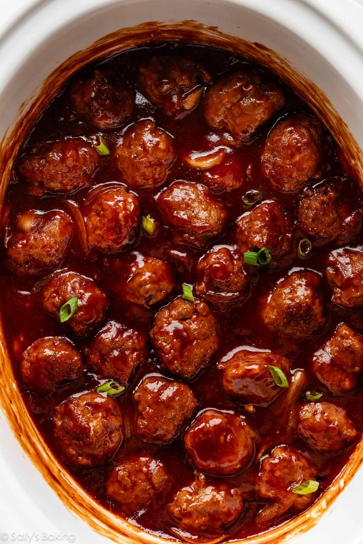 meatballs in bbq sauce in slow cooker with green onion garnish.
