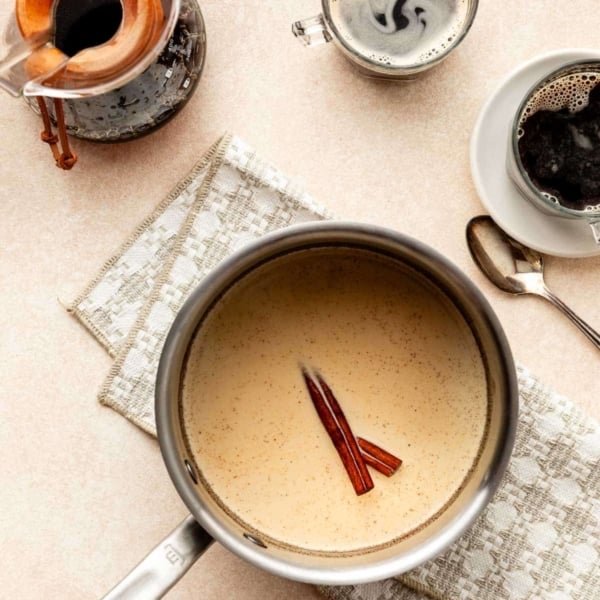 cream mixture in pot with cinnamon sticks on beige-patterned linen.