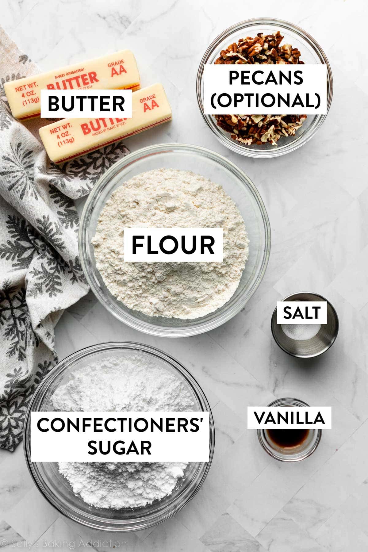 ingredients on counter including flour, pecans, butter, salt, vanilla, and confectioners' sugar.