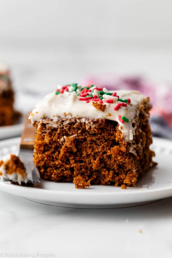 slice of gingerbread snack cake with cream cheese frosting and sprinkles on top on white plate.
