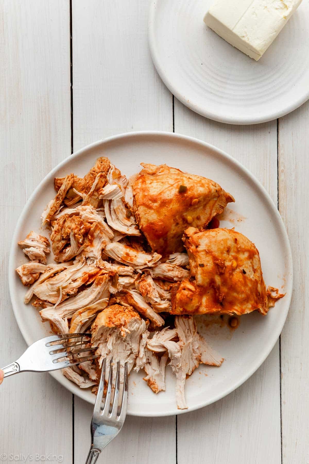 forks shredding chicken on white plate.