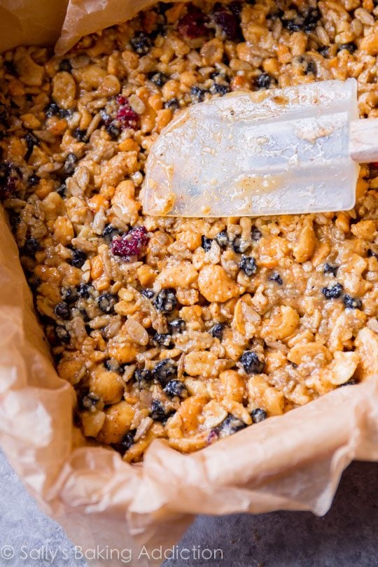 pressing snack bar mixture in a parchment paper lined pan with a spatula