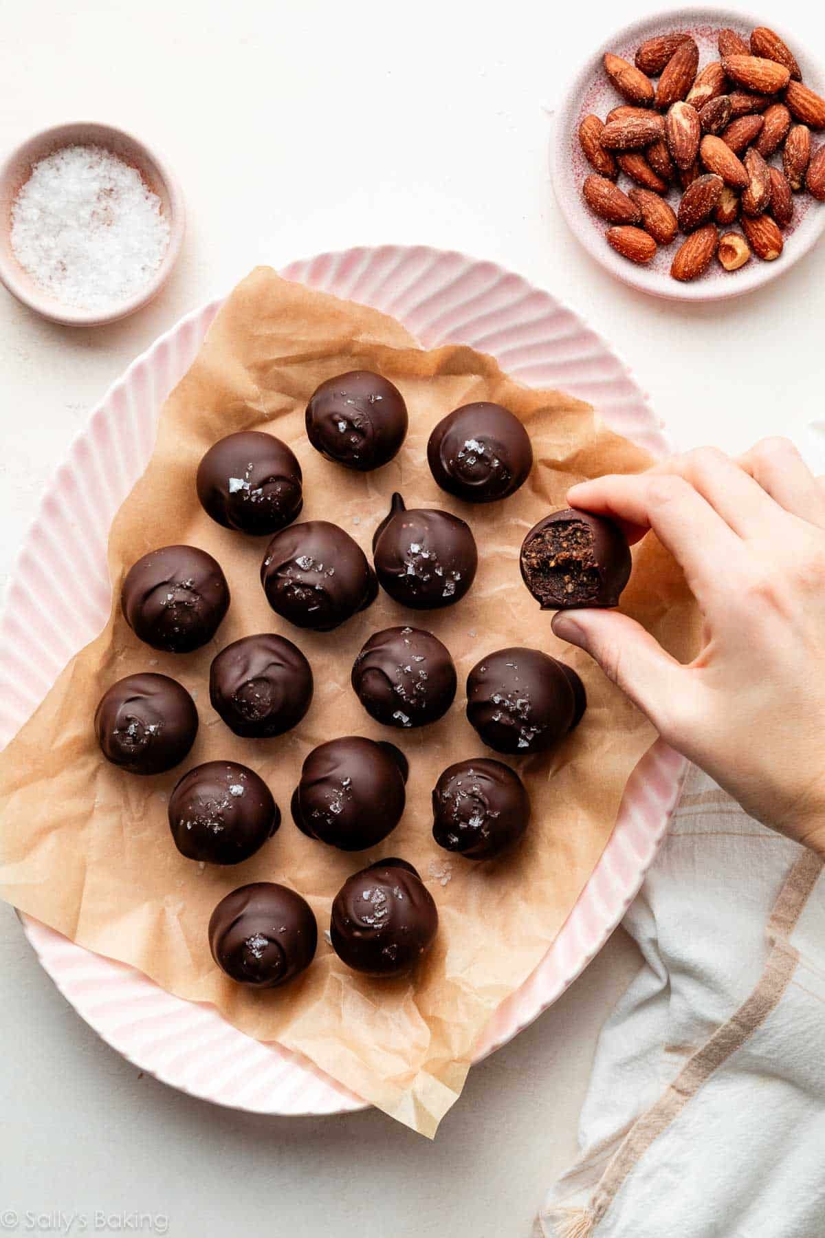 hand grabbing a chocolate date and almond truffle off of a pink plate.