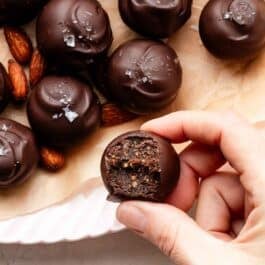 hand holding a bitten chocolate date and almond truffle.