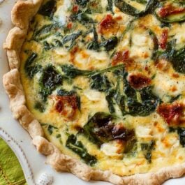 goat cheese spinach sun-dried tomato quiche in a white pie dish