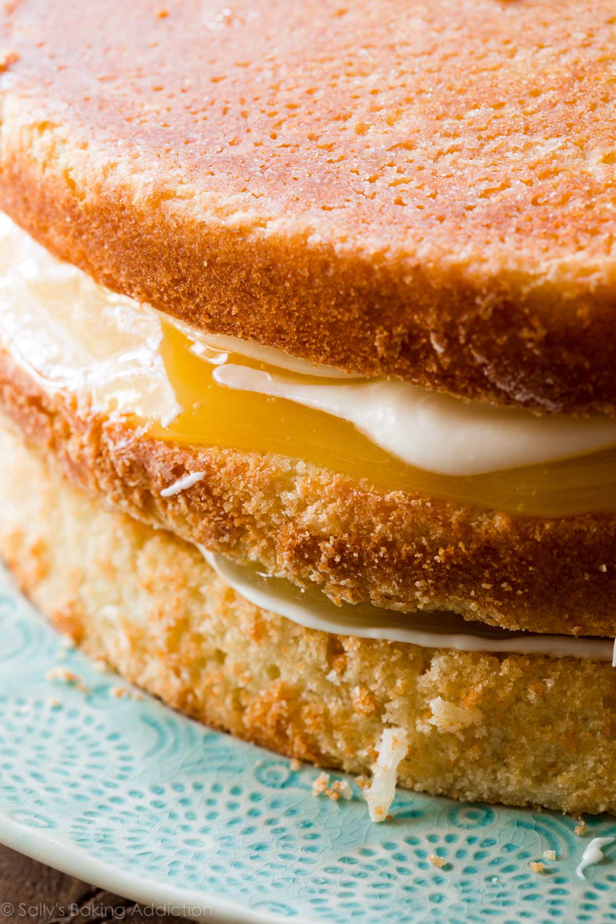 cream cheese frosting and lemon curd in between layers of coconut cake on a teal plate