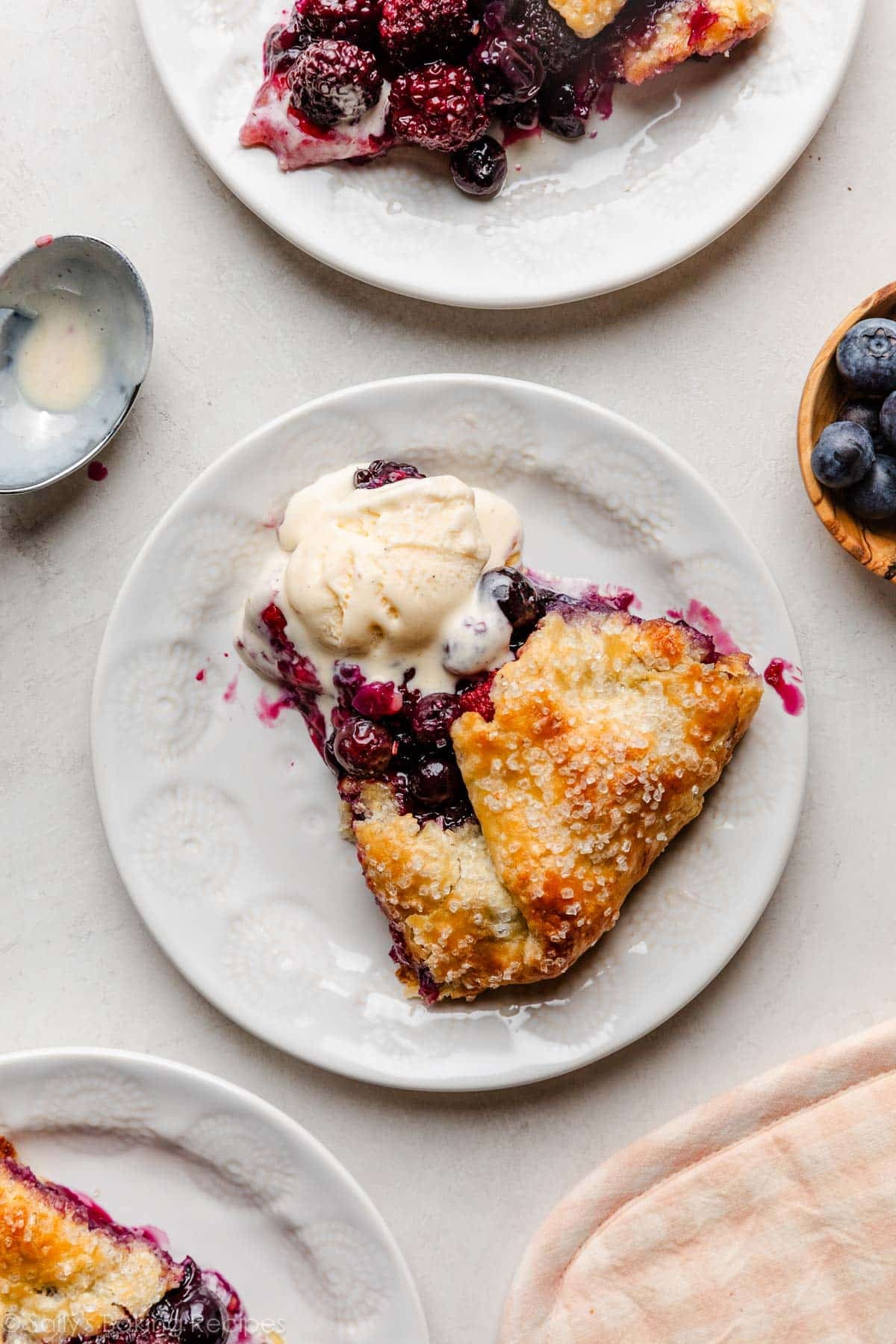slice of berry galette on white plate with melted vanilla ice cream on top.