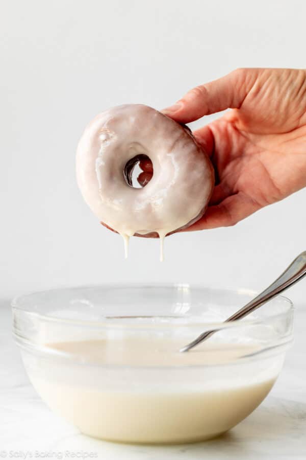 hand holding doughnut dropping glaze into glass bowl of icing.