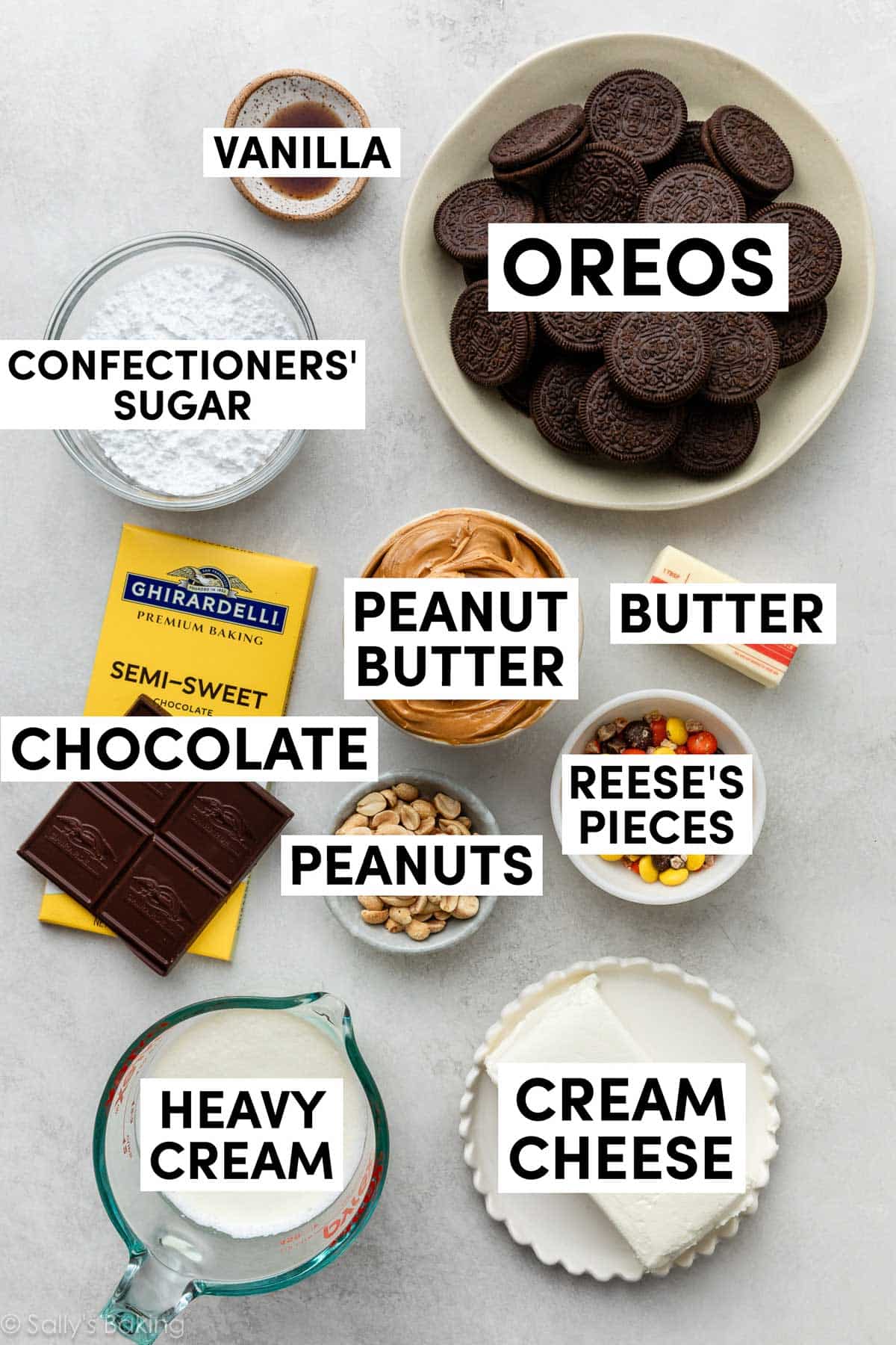 ingredients on white surface including peanuts, cream cheese, chocolate, heavy cream, confectioners' sugar, Oreos, and butter.