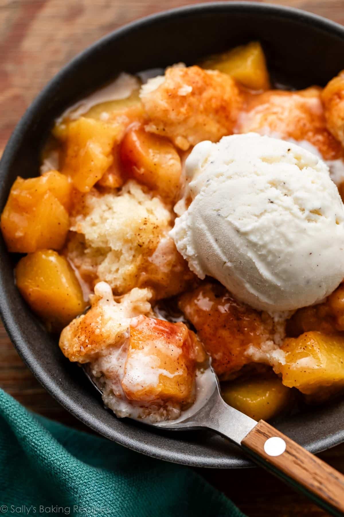 biscuit peach cobbler in bowl with ice cream and spoon removing a bite.