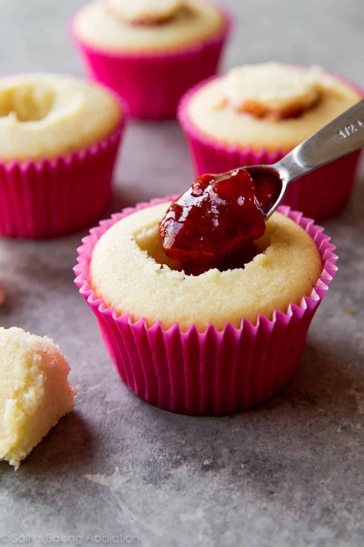 spooning jelly into vanilla cupcakes