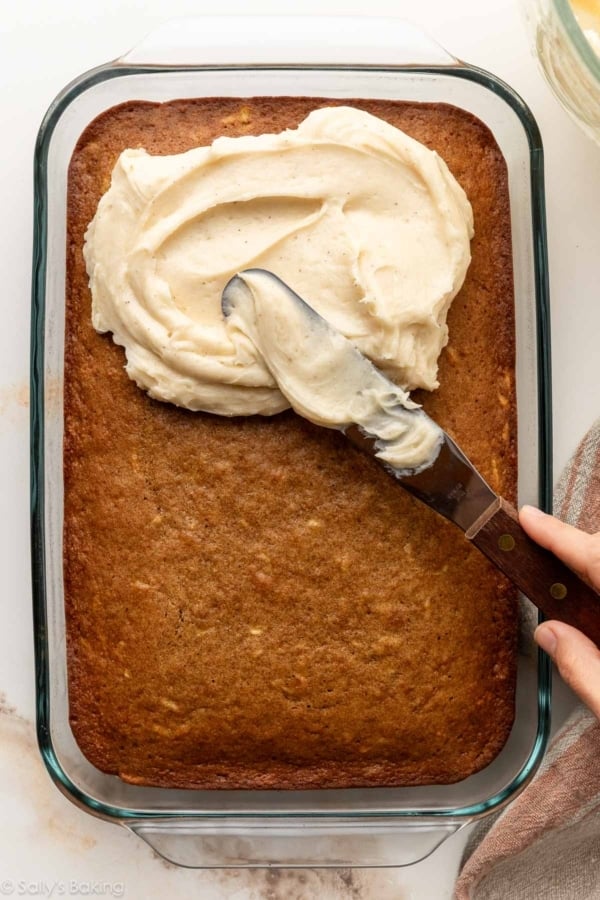 spreading frosting on quarter sheet cake in glass dish.