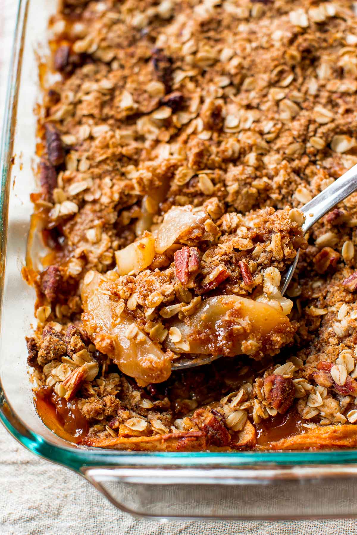 apple pear crisp in a glass baking dish with a serving spoon