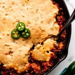 serving spoon spooning cornbread chili casserole out of a black cast iron skillet.