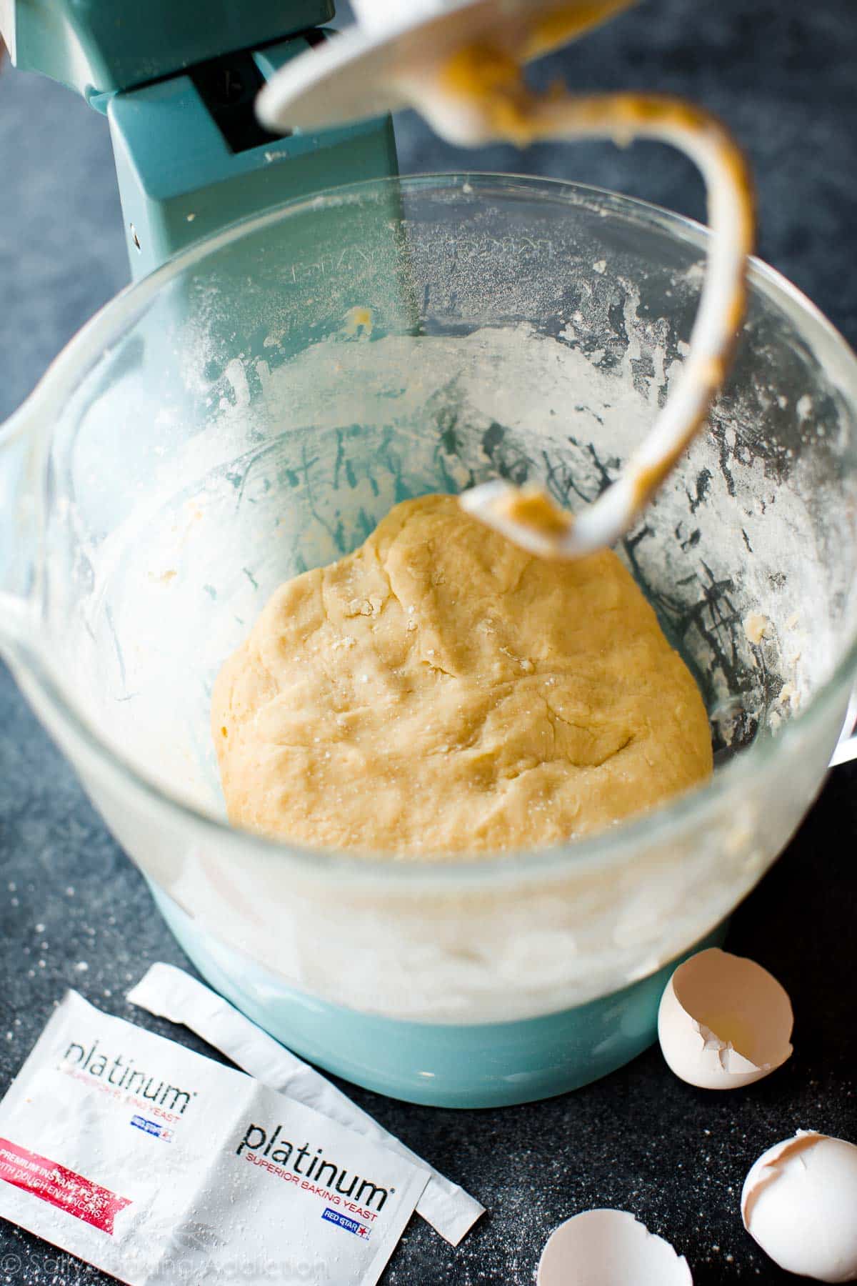 cinnamon roll dough in a glass stand mixer bowl with a hook attachment